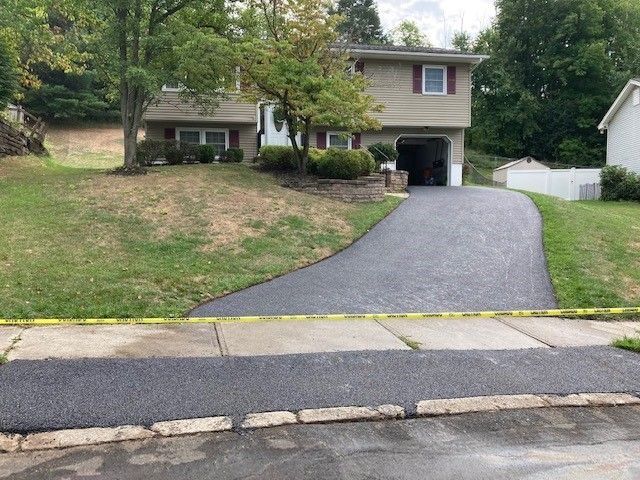 A beige split-level house with a newly paved asphalt driveway and a yellow caution tape strung across the front.