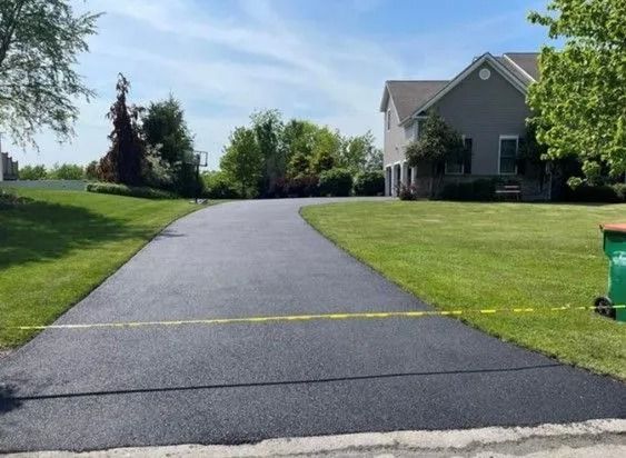 A freshly paved dark asphalt driveway leads toward a house, sectioned off by yellow caution tape.