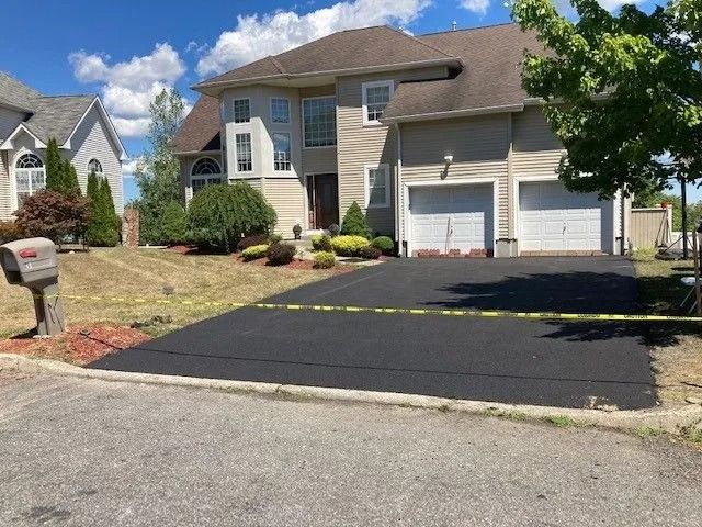 A suburban two-story house with a newly paved asphalt driveway cordoned off with yellow caution tape.