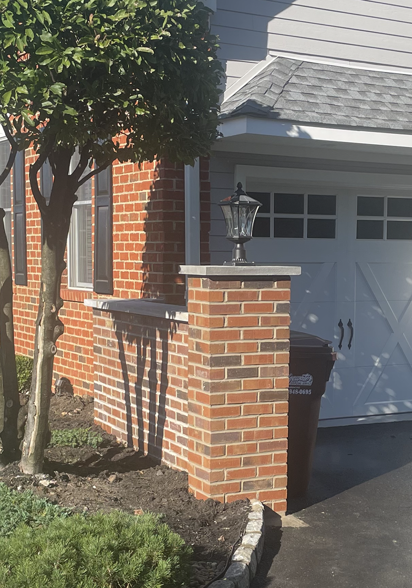 A brick pillar in front of a house with a white garage door