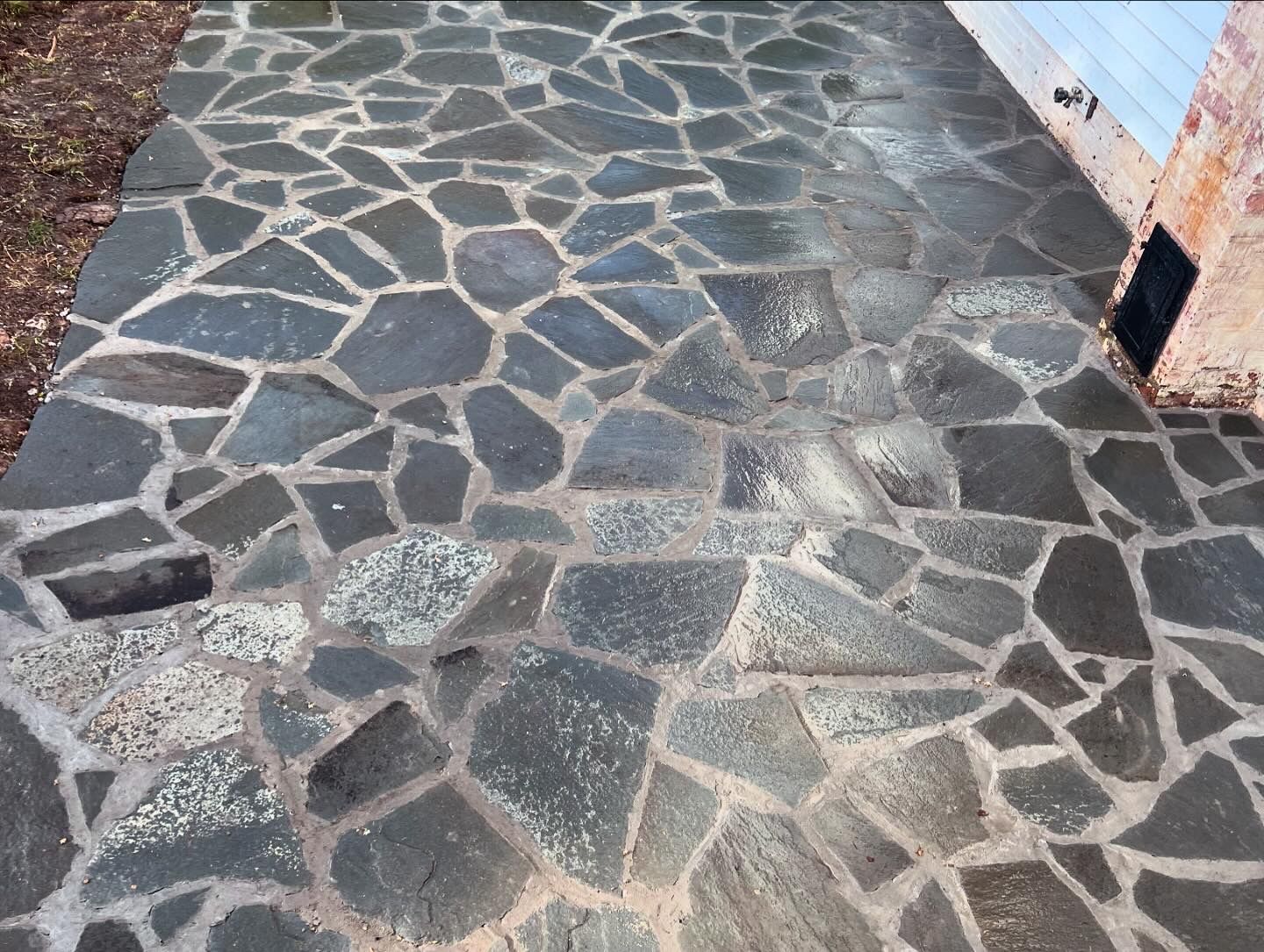 A stone walkway leading to a house with a blue building in the background.