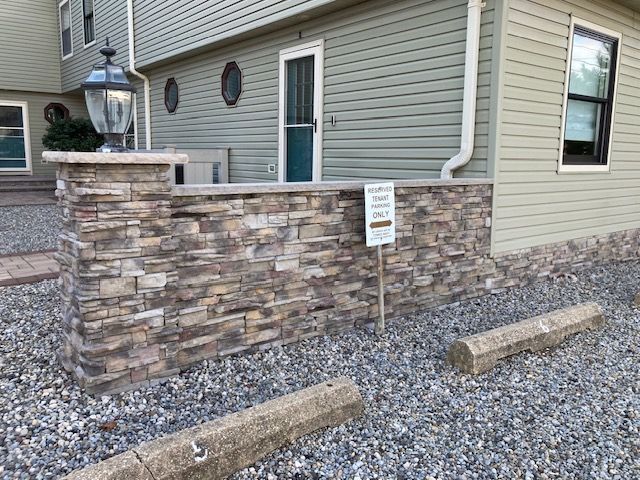 A house with a stone wall and a parking lot in front of it.