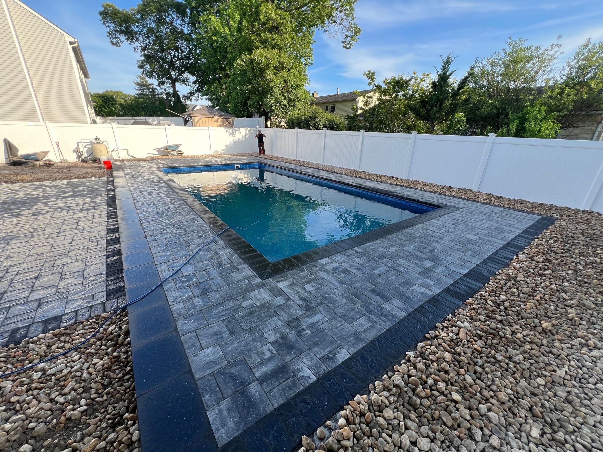 A large swimming pool in a backyard with a white fence surrounding it.
