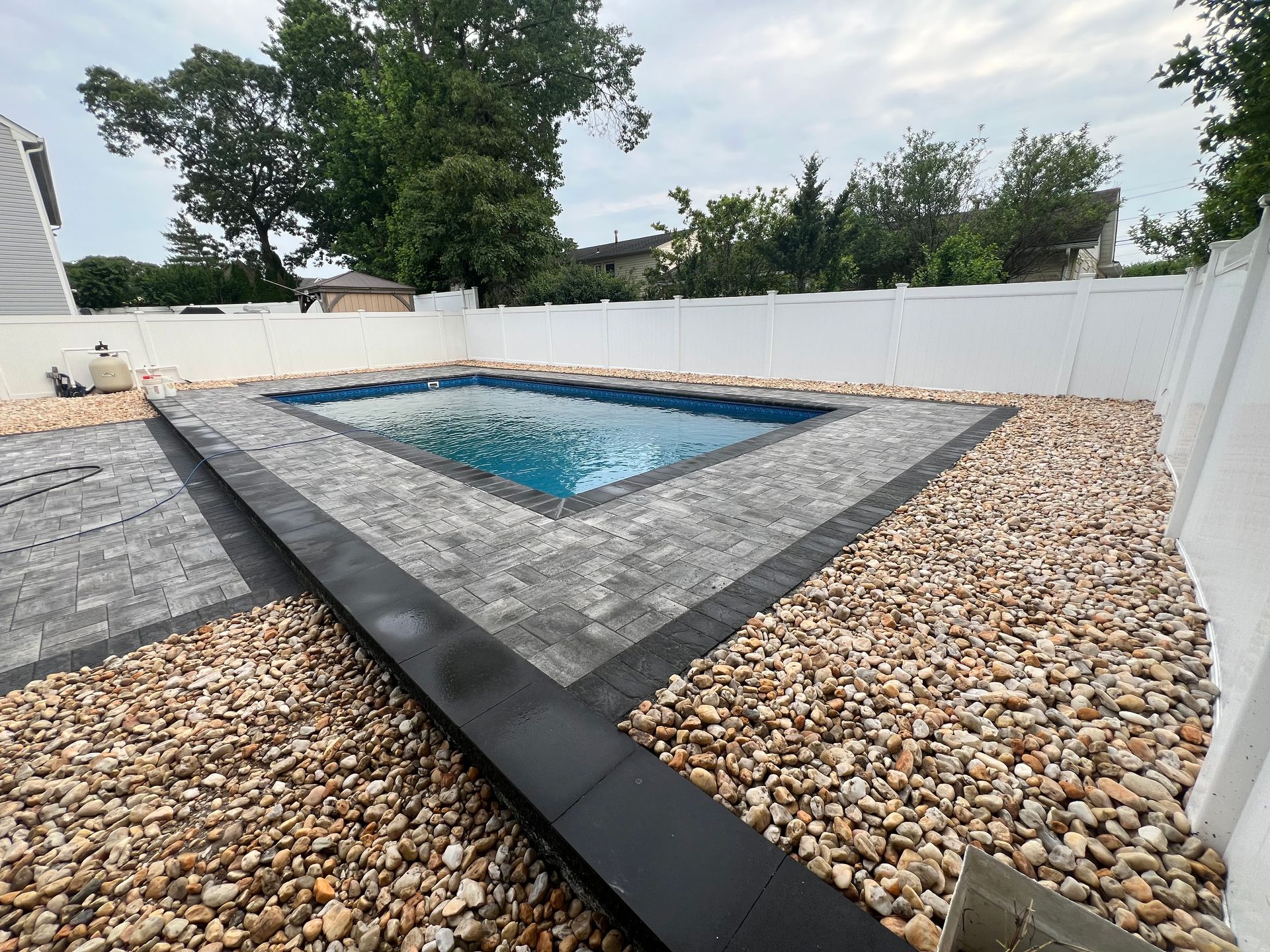 A swimming pool is surrounded by gravel and a white fence.