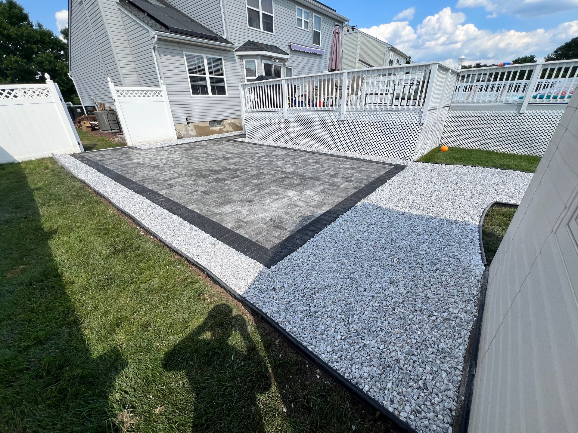 A backyard with a concrete walkway leading to a deck and a house.