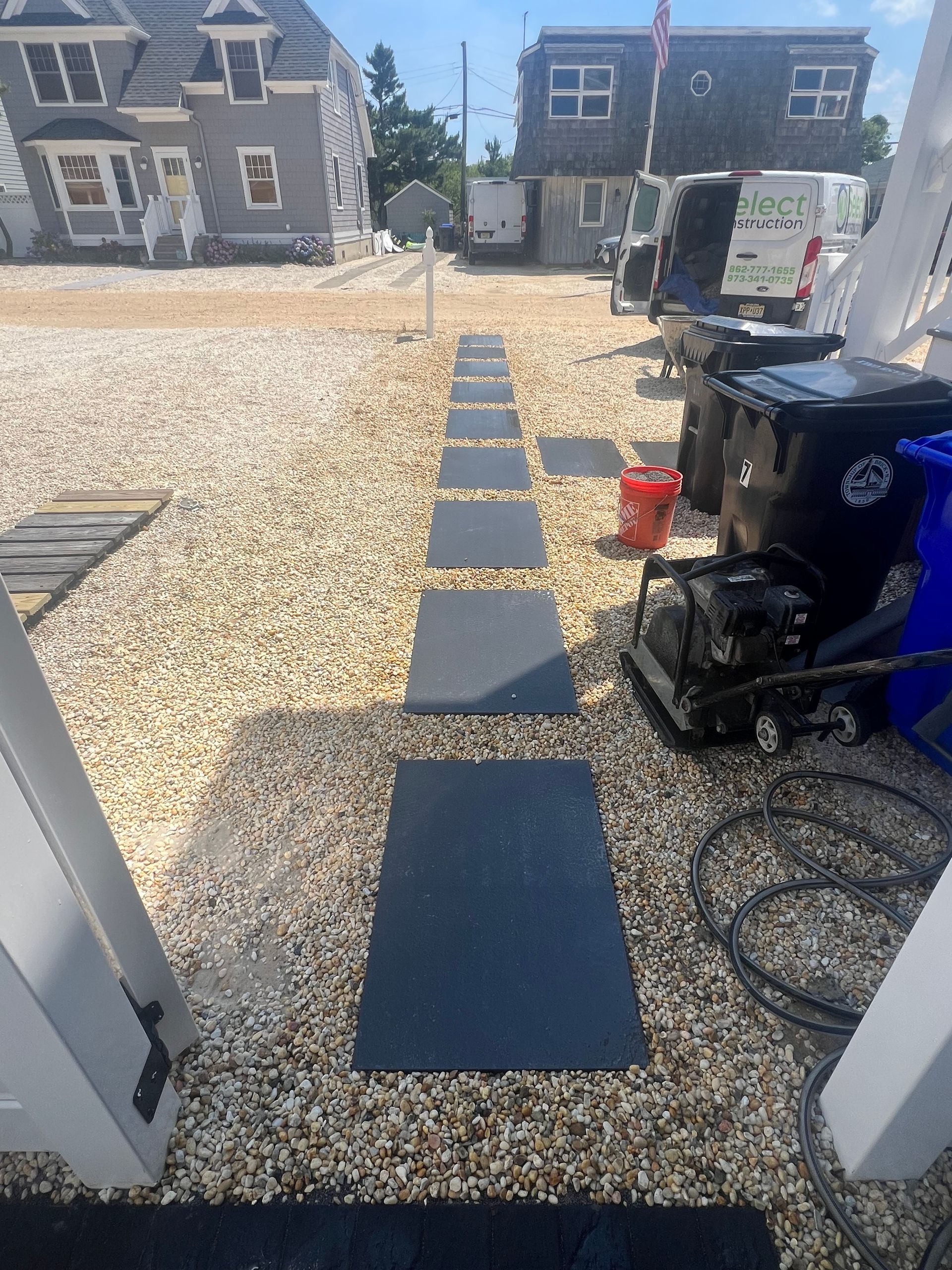 A row of black tiles on a gravel path leading to a house.