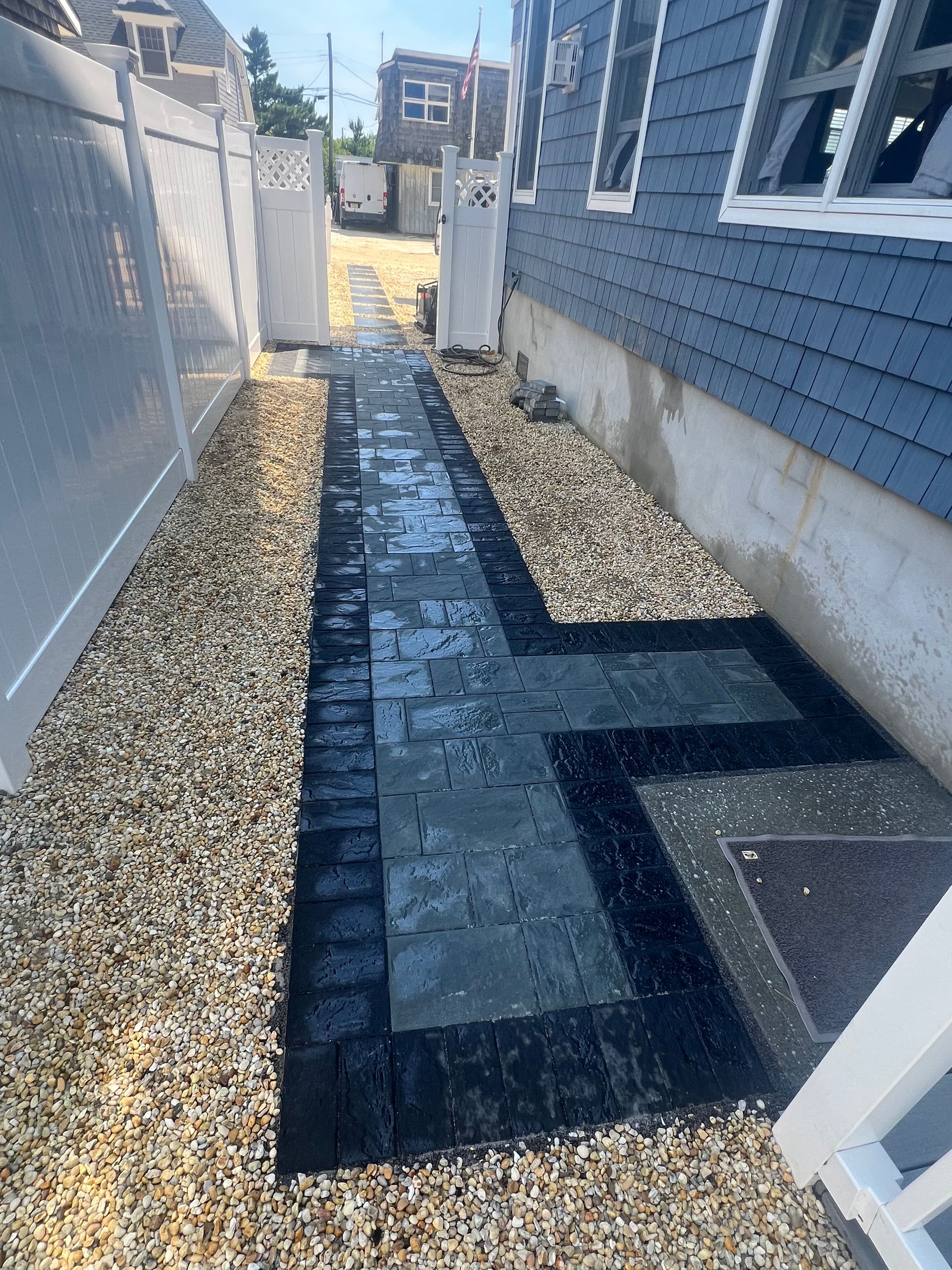 A walkway leading to a house with a white fence and gravel.