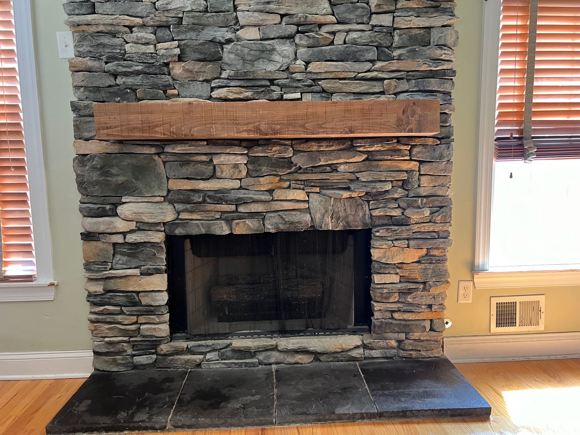 A stone fireplace with a wooden mantle in a living room