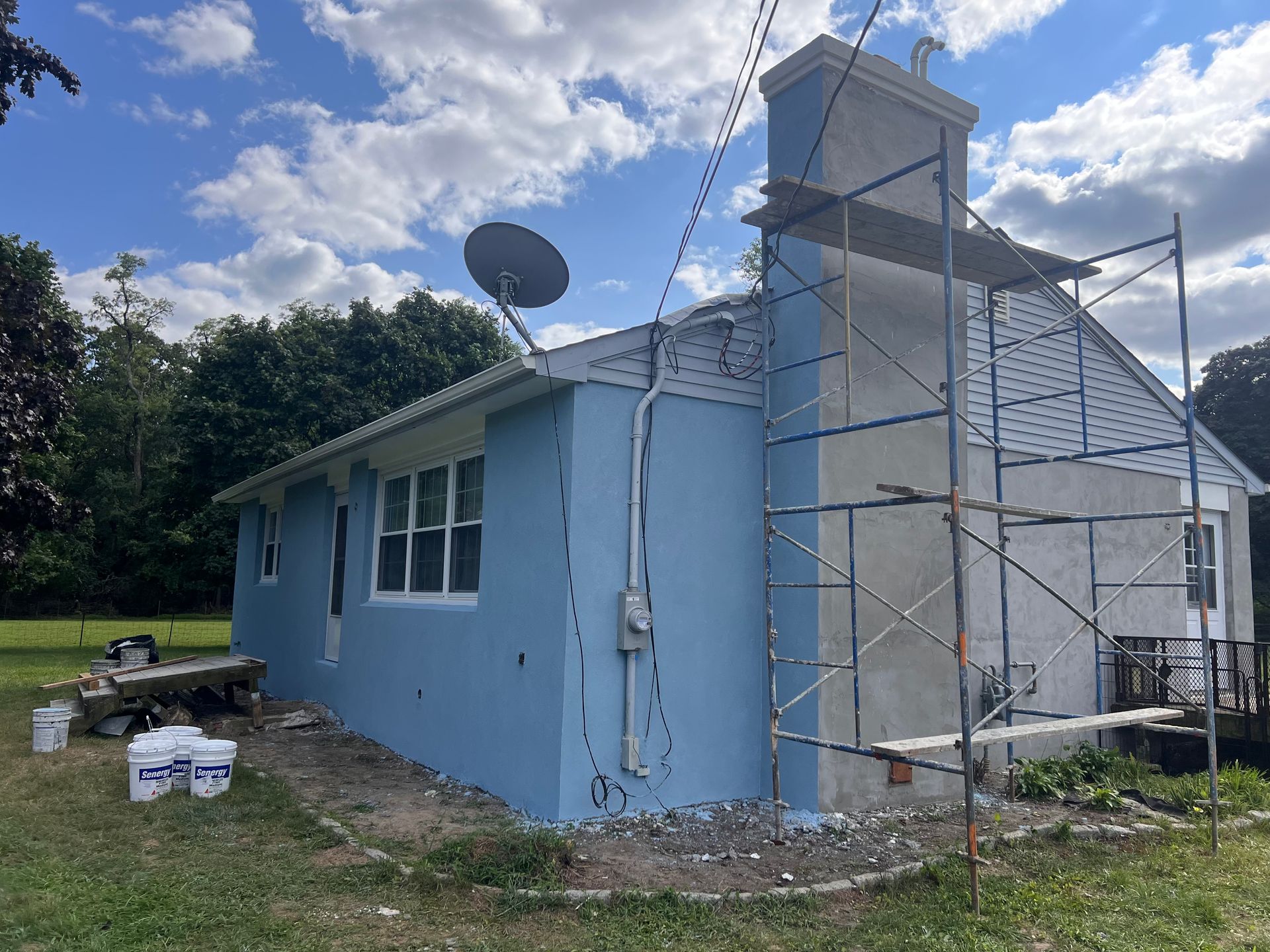 A blue house is being painted with a scaffolding in front of it.