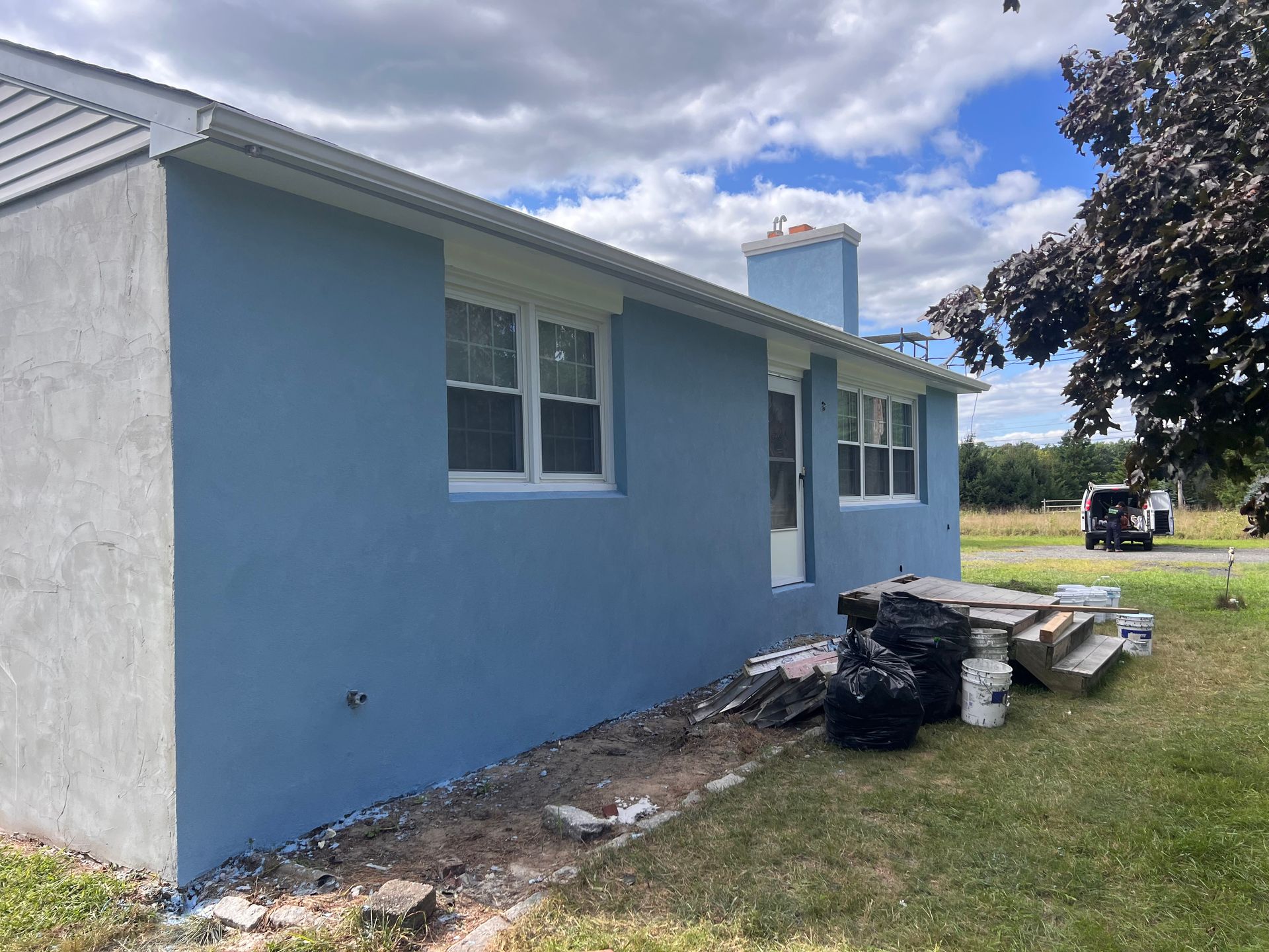 A blue house is sitting in the middle of a grassy field.