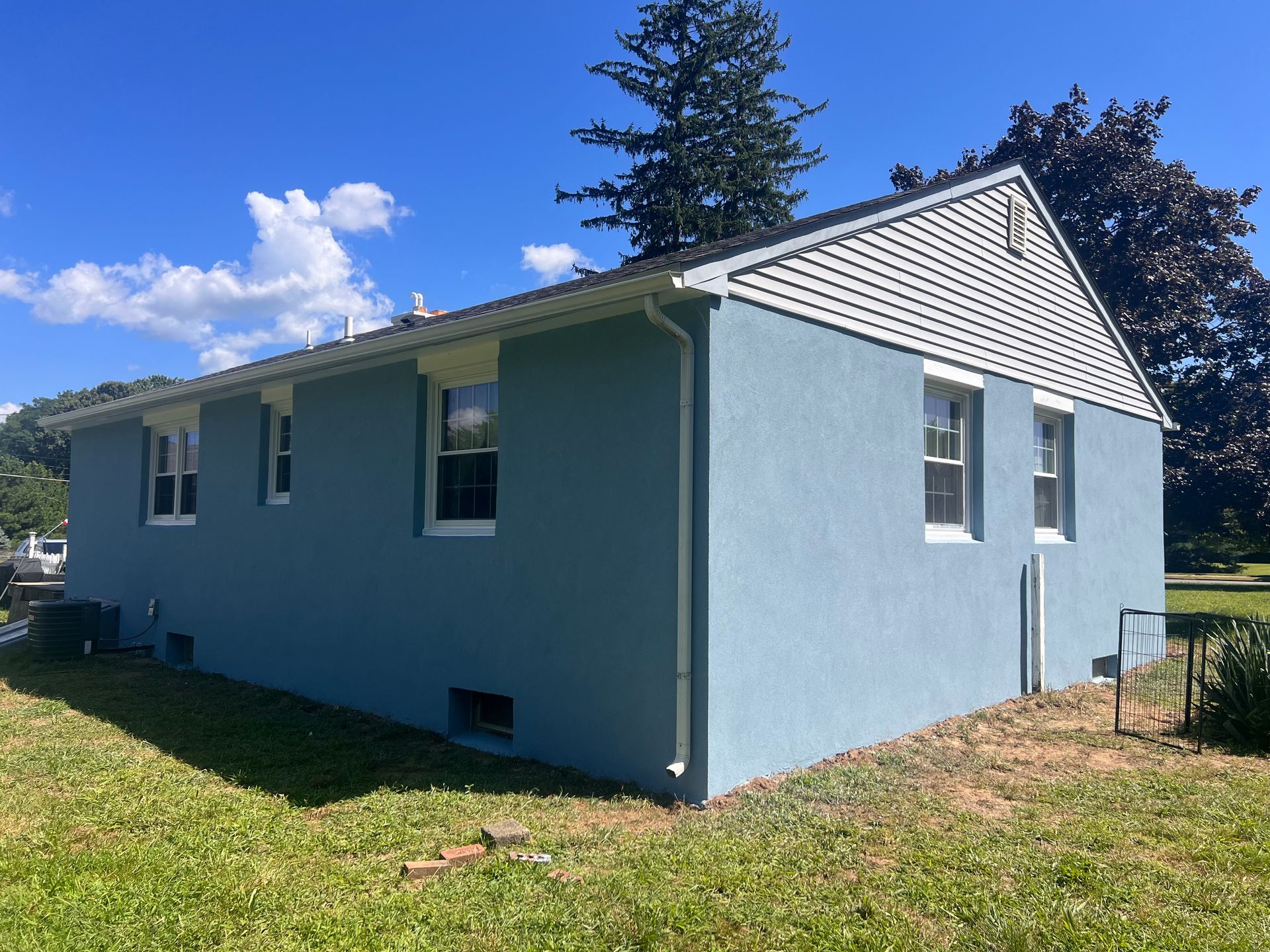 A blue house with white trim is sitting in the middle of a lush green field.