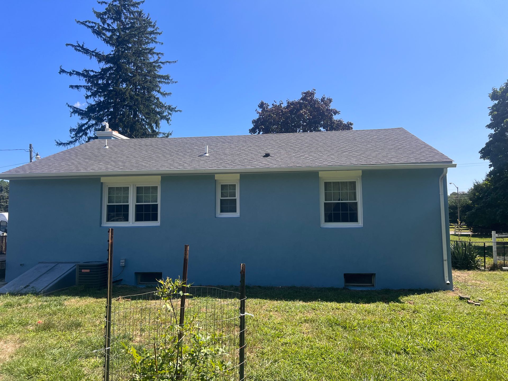 A blue house with a gray roof is sitting in the middle of a grassy field.