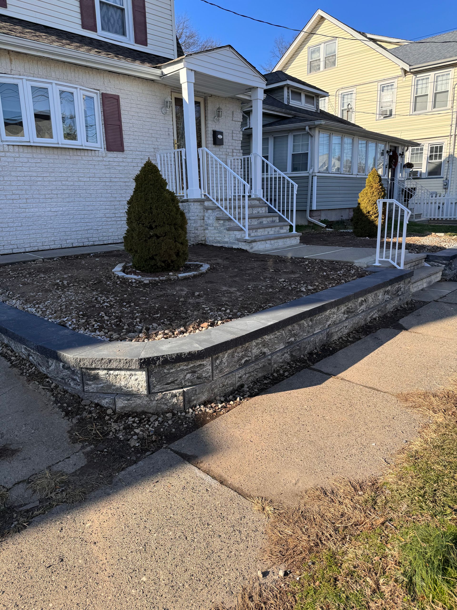 A white house with stairs and a stone wall in front of it.