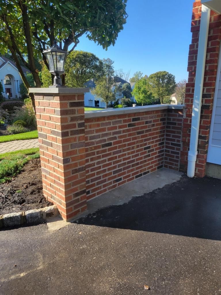 A brick wall with a lamp on top of it in front of a house.
