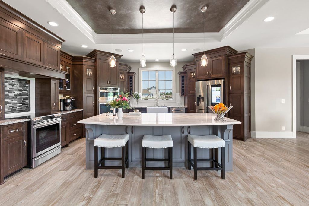A spacious kitchen with dark wood cabinetry, a large gray island with three stools, and a dark recessed ceiling.
