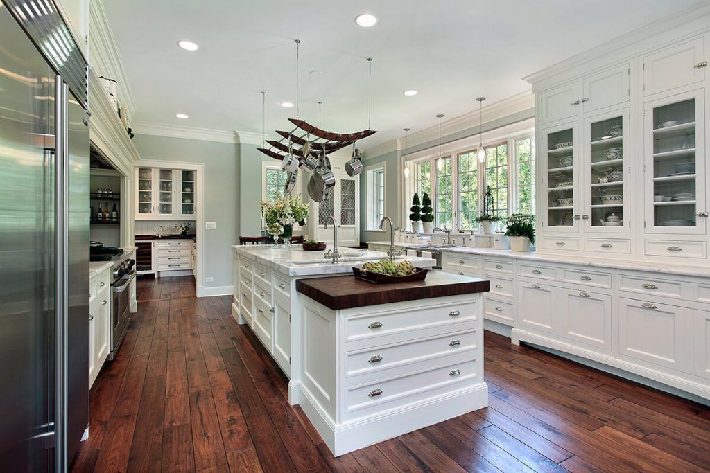 Bright white kitchen featuring a large central island with a dark wood countertop and dark wood floors.