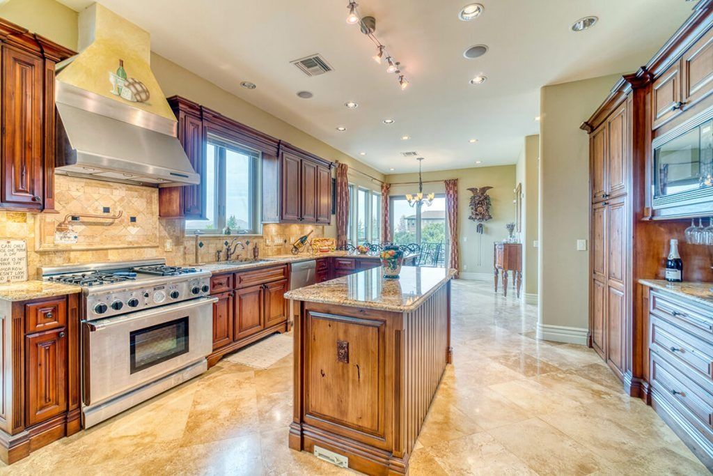 A spacious kitchen with wood cabinets, stainless steel appliances, a large center island, and tiled flooring.