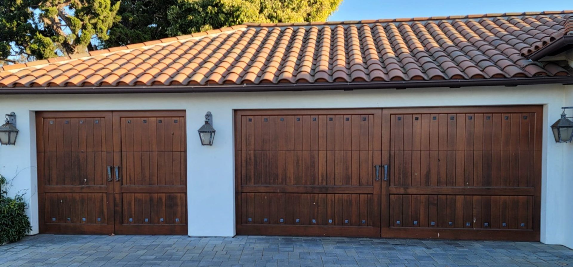 Three dark wooden garage doors with matching lights and a terracotta tile roof.