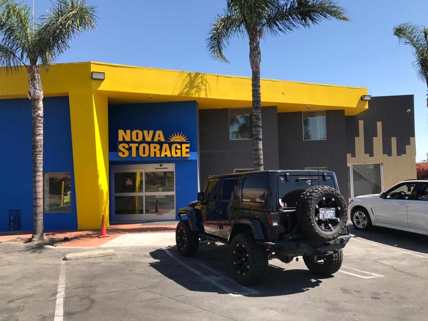 Nova Storage building with yellow and blue facade, black Jeep parked out front, palm trees.