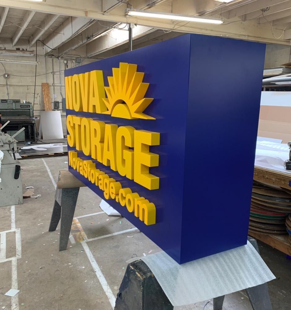 Blue and yellow illuminated sign for Nova Storage; in workshop.