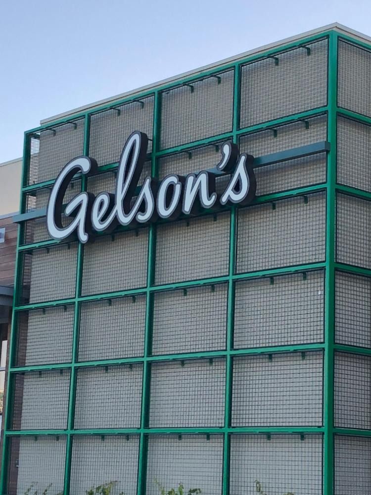 Gelson's grocery store sign on a green grid facade, white script on dark background.