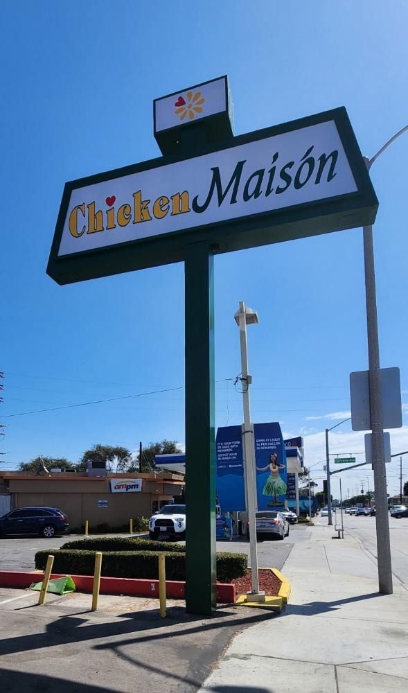 Sign for Chicken Maison, a restaurant. The sign is green and white, with the restaurant's name. A clear blue sky is in the background.
