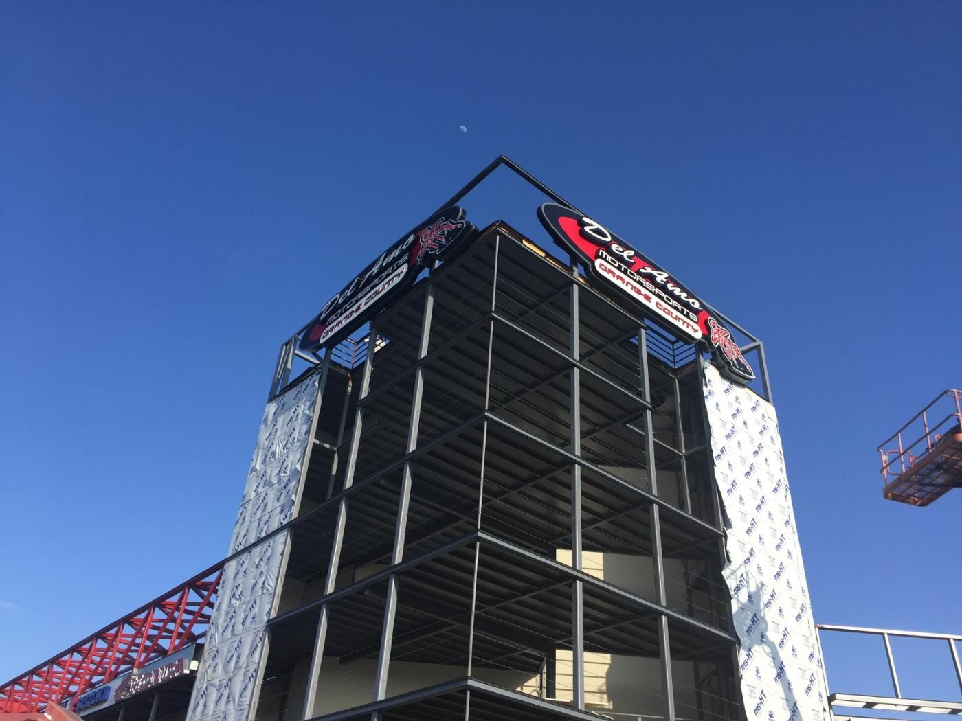 Steel frame of a building under construction, with signage at top against blue sky.