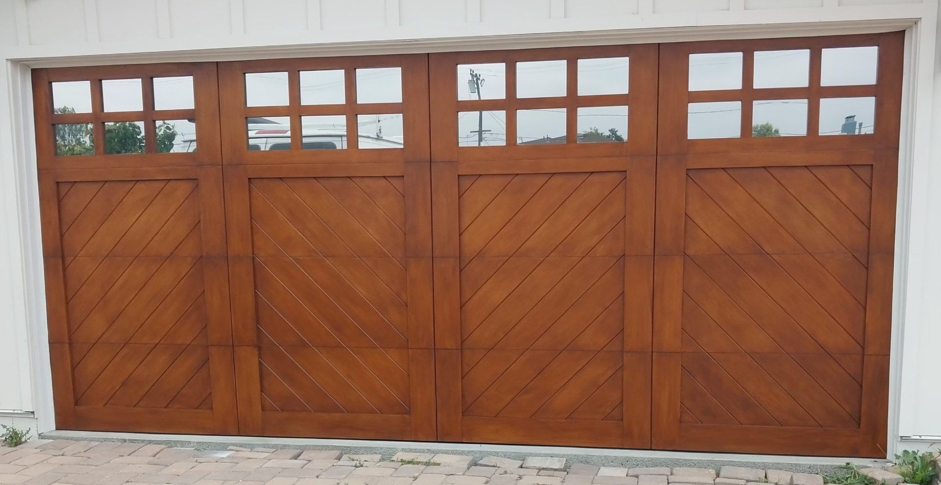 Four-panel wooden garage door with diagonal lines and glass windows across the top.