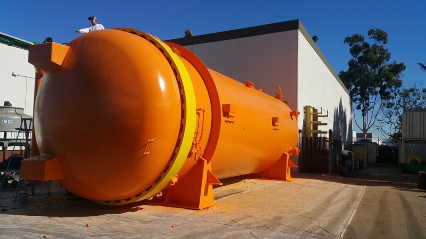 Large orange cylindrical tank with yellow accents, outdoors near a building.