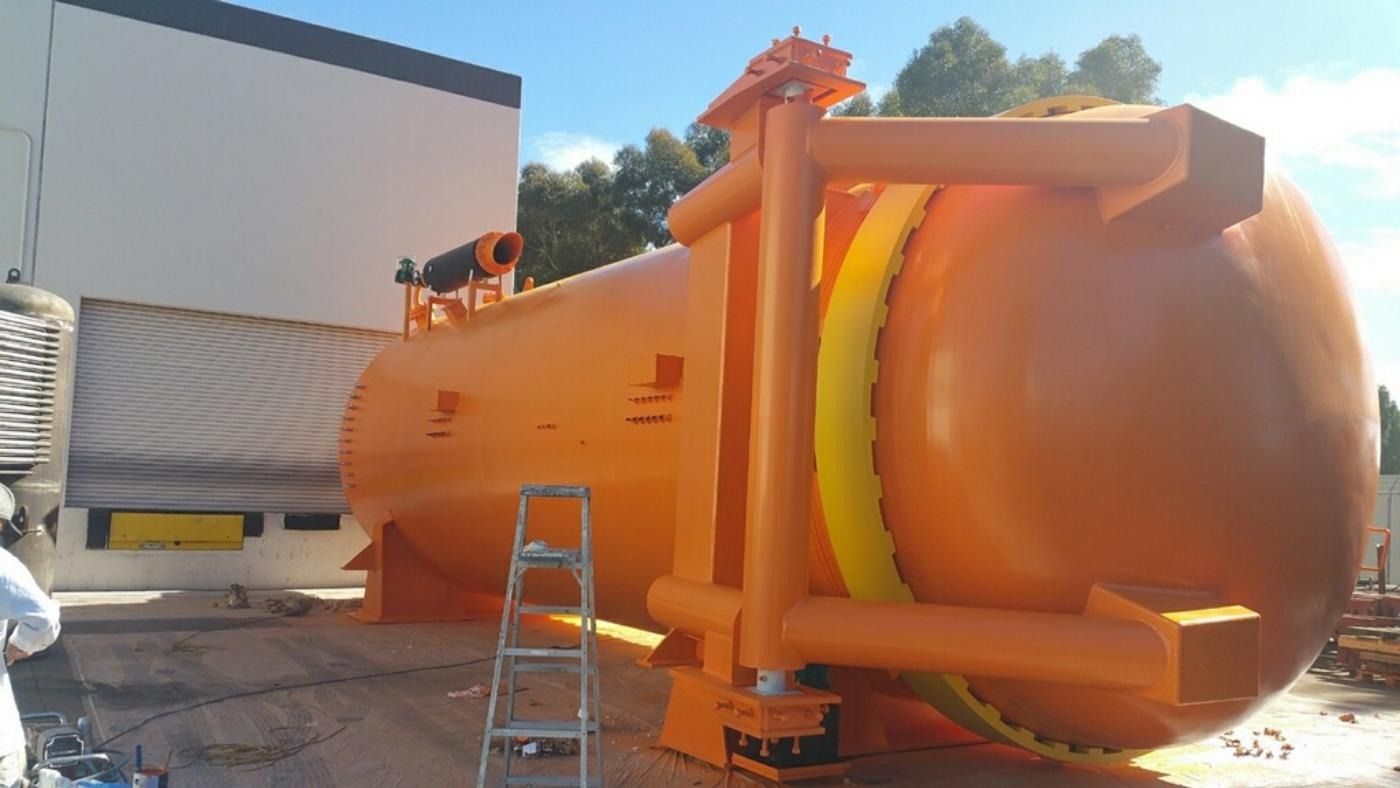 Orange industrial tank with yellow supports, outside a building.