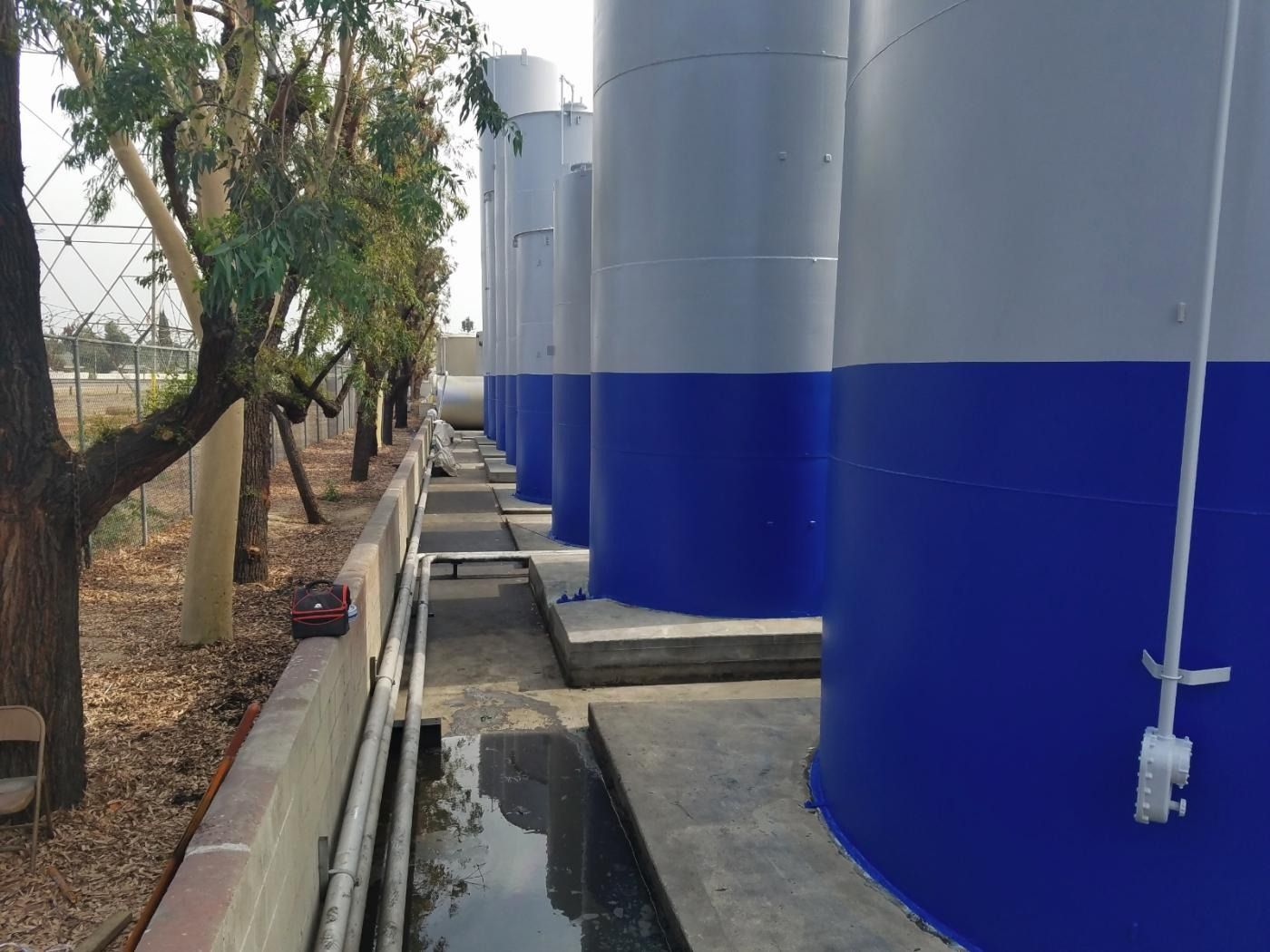 Row of blue and white storage tanks in an industrial setting, with a concrete walkway.