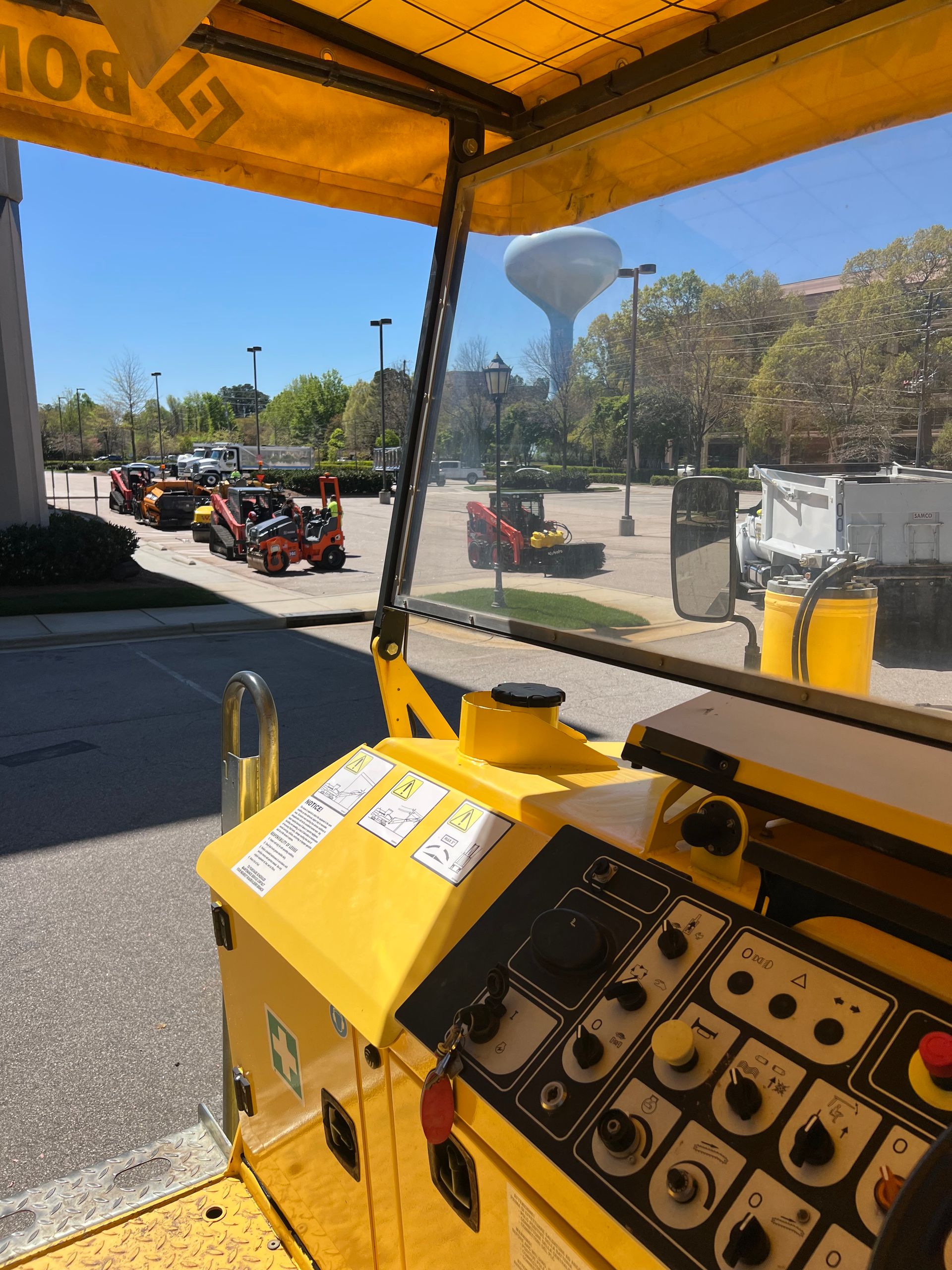 A yellow tractor is parked in a parking lot with a water tower in the background