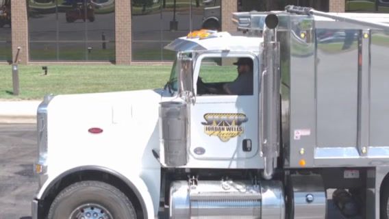 A dump truck is parked in a parking lot in front of a building.
