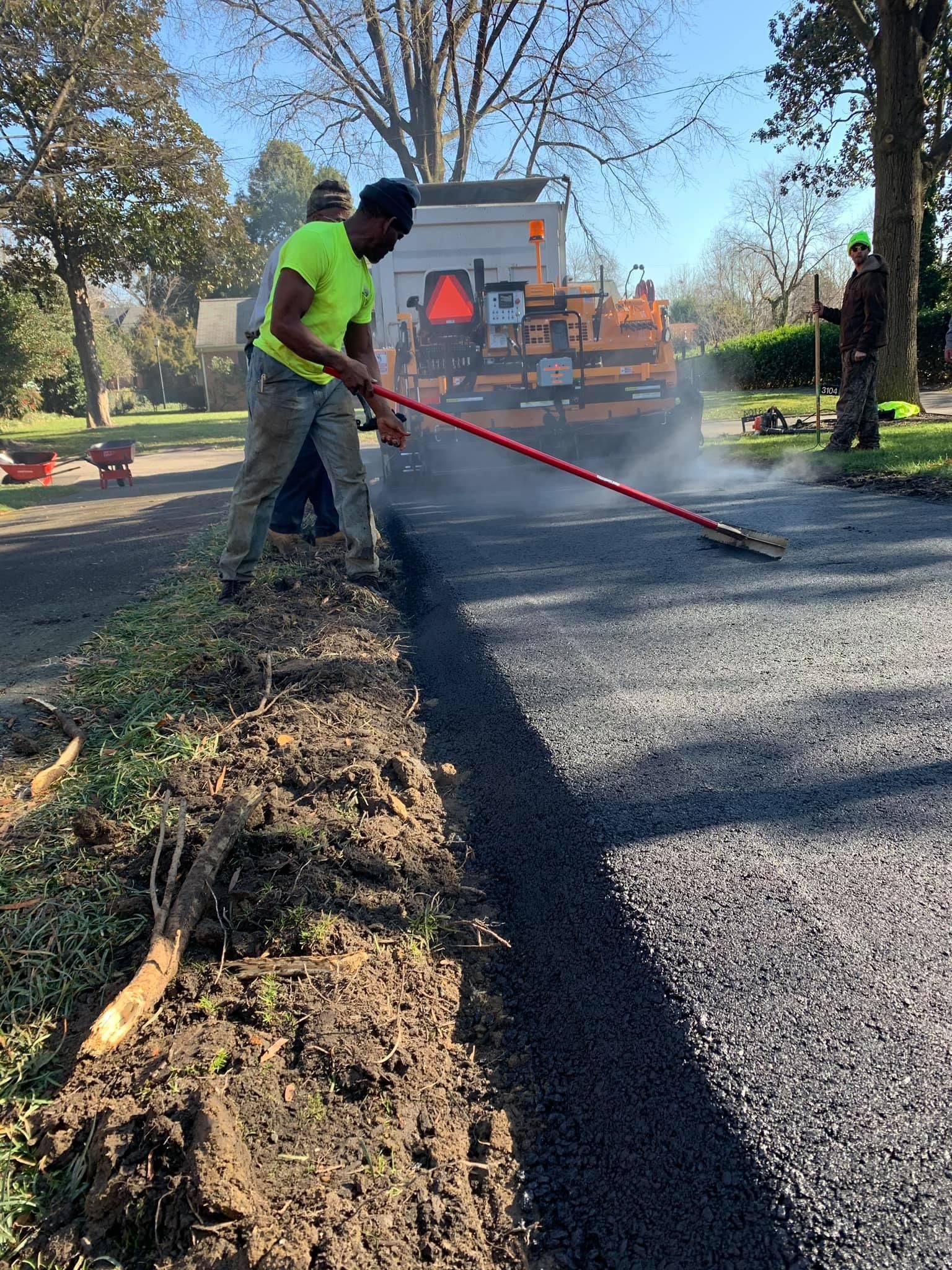 A man is using a rake to spread asphalt on a road.