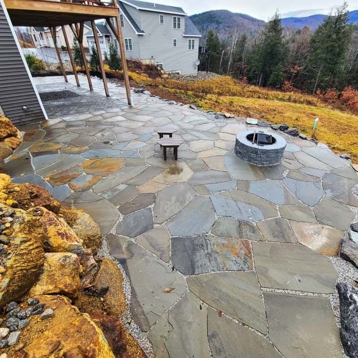 Flagstone patio with fire pit, small wooden chair, and hillside in background.