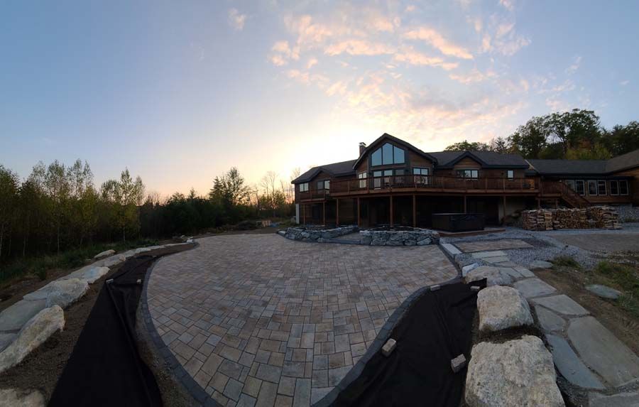 Large wooden house with expansive stone patio; dusk setting with colorful sky.