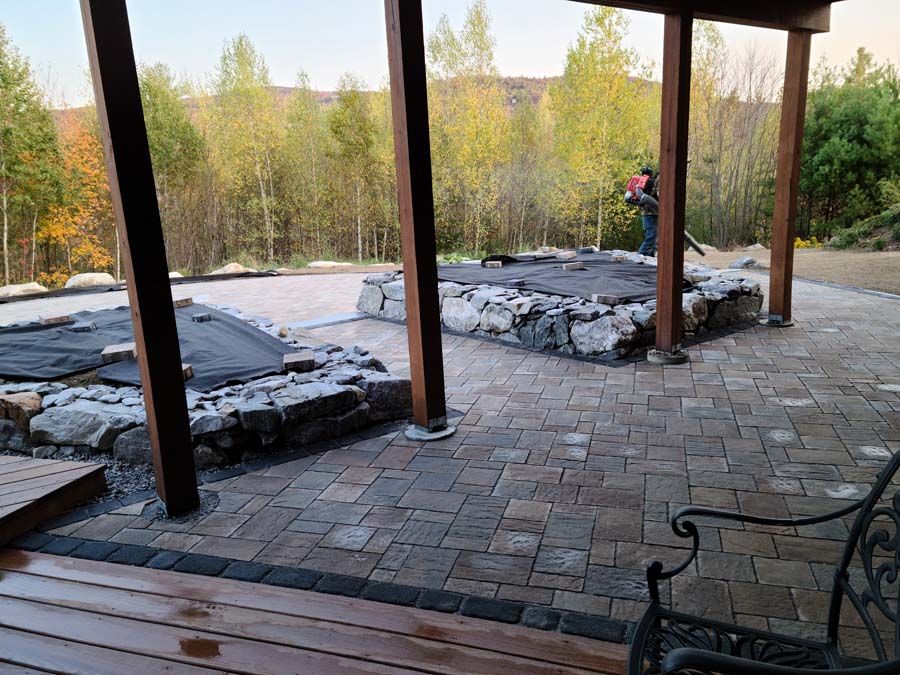 Brick patio with stone planters, a person blowing leaves, trees in the background.