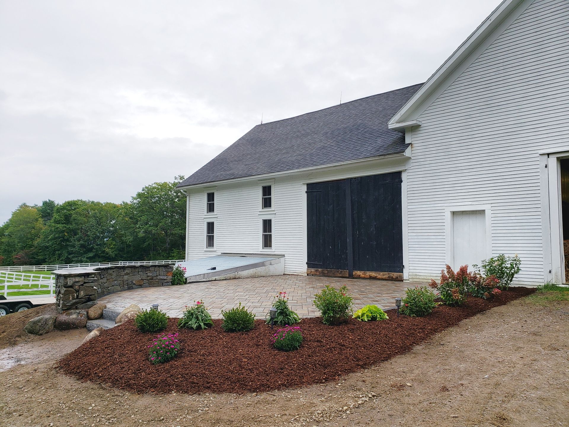 White barn with black doors and a small garden bed in front.