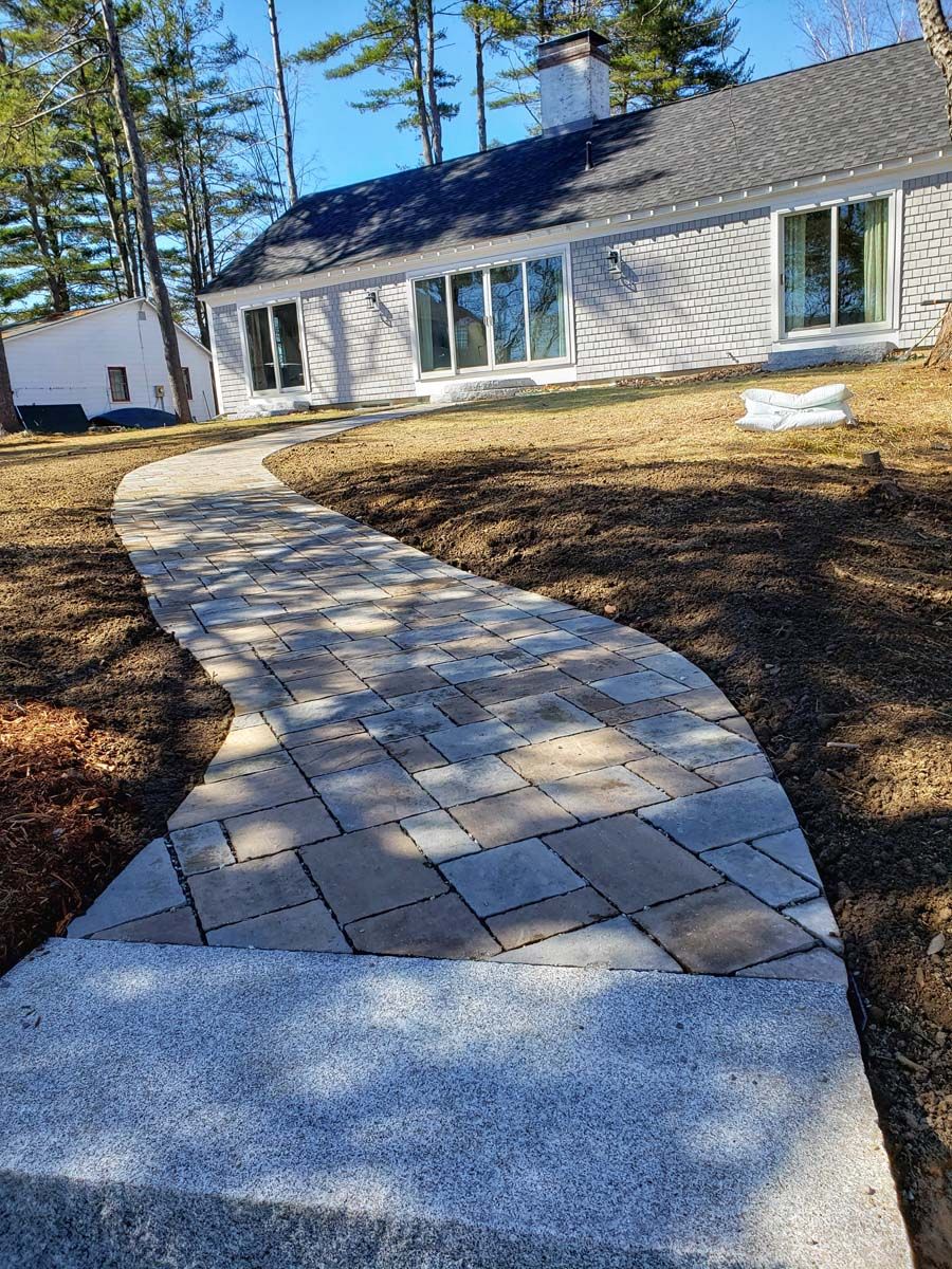 Stone walkway curves toward a house with large windows.