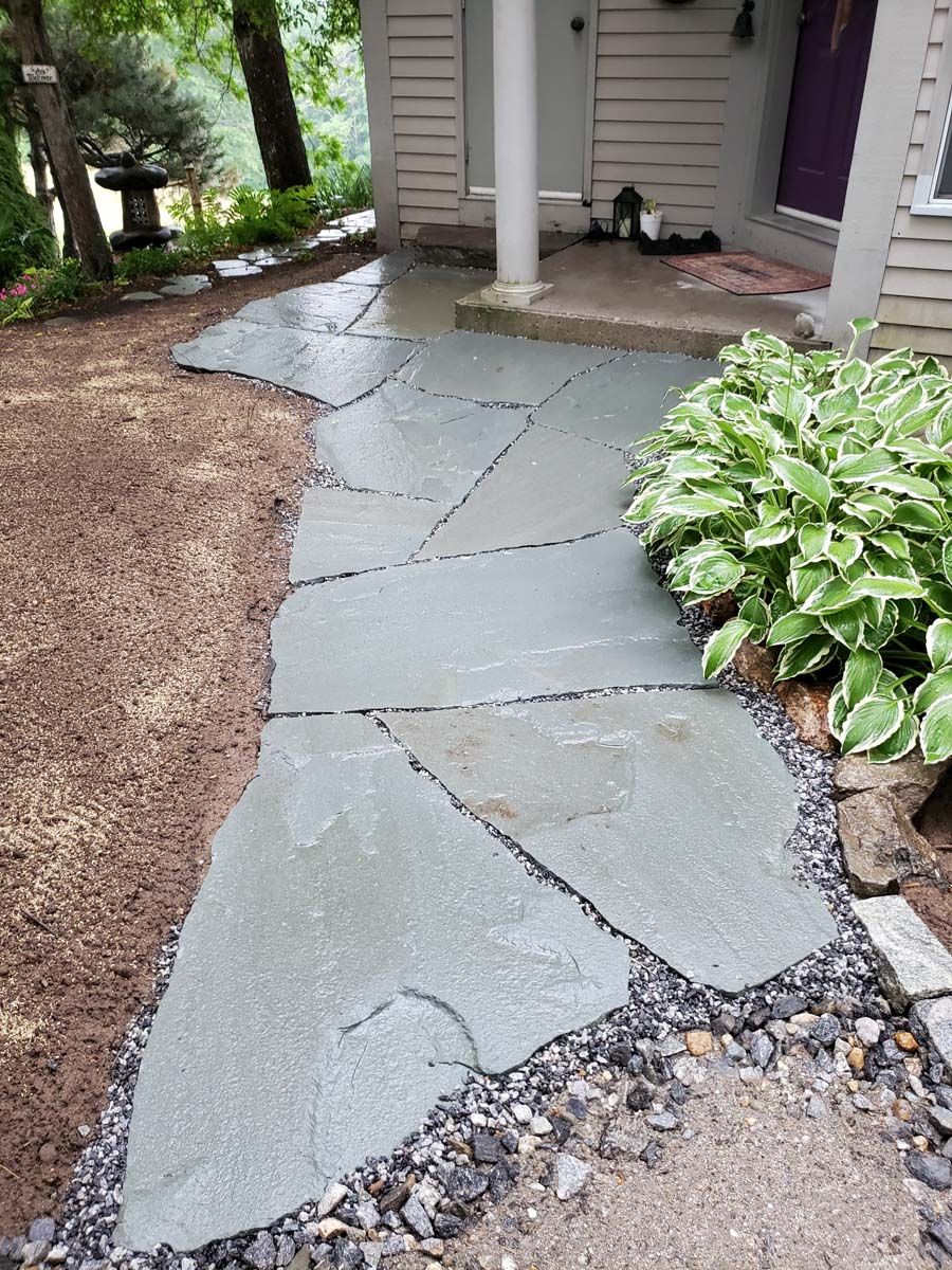 Stone path leading to a house entrance, surrounded by landscaping with gravel.