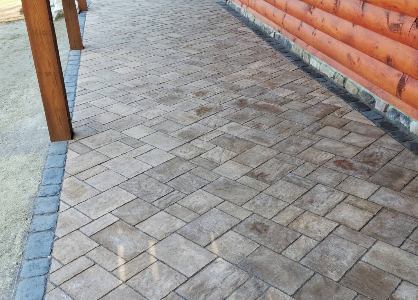 Paver walkway alongside a log cabin, bordered by a darker row of stones.