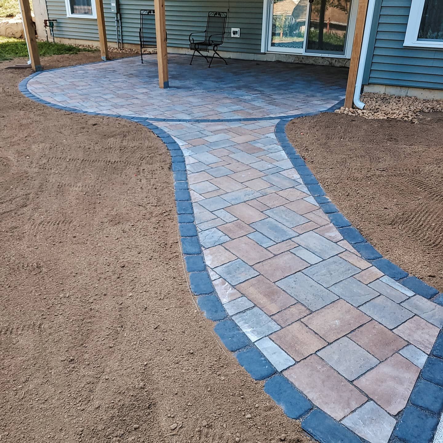 Brick patio and walkway leading from a blue house to an outdoor seating area with a wooden pillar.