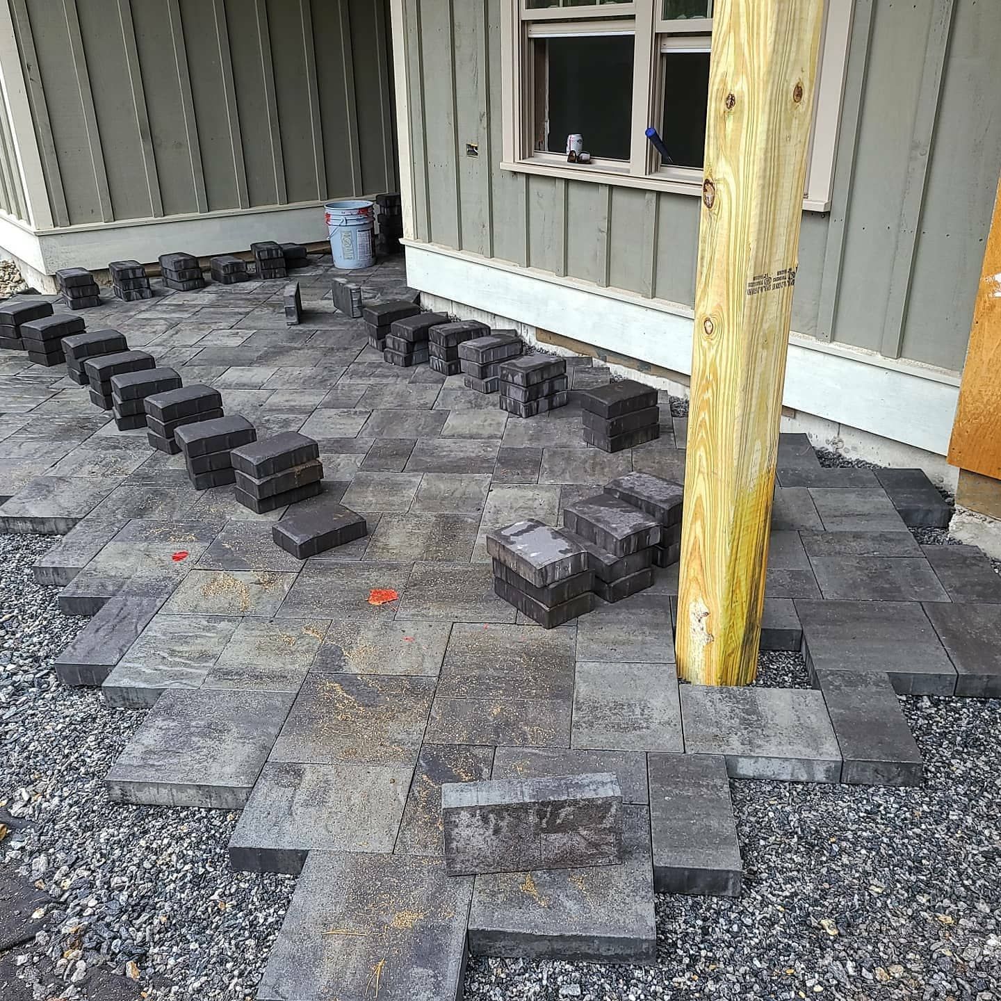 Patio construction with gray pavers, gravel, and a wooden support beam next to a house.
