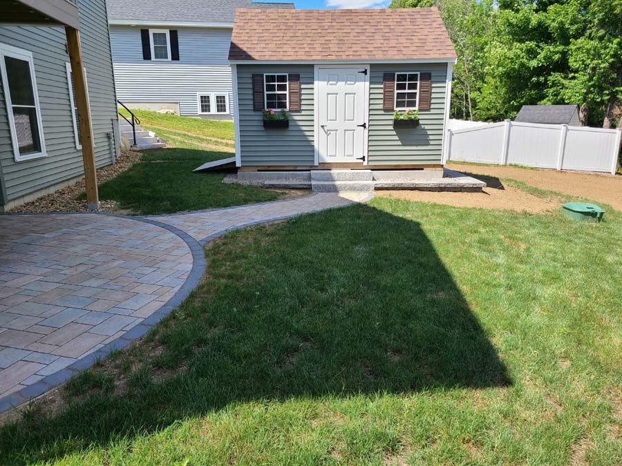Backyard with lawn, stone patio, shed, and pathway leading to the shed door.