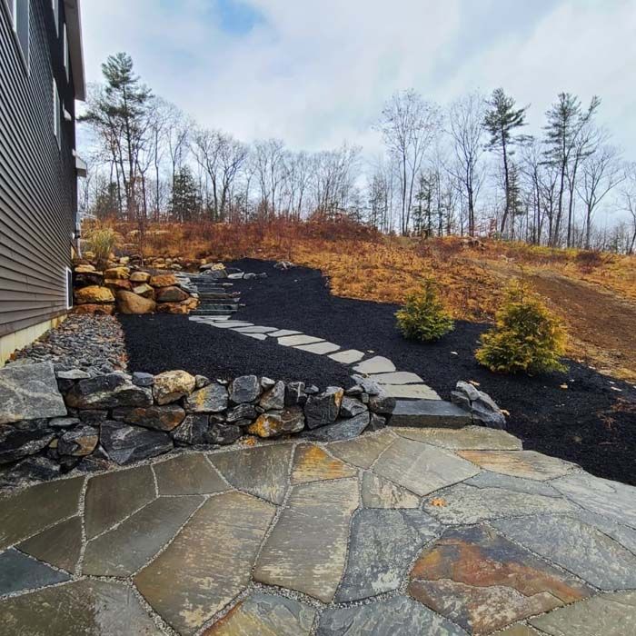 Stone patio with steps leading uphill through mulch; trees in background.