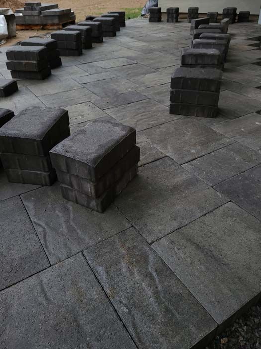 Pavers being installed on a patio, dark grey blocks stacked, setting appears to be outdoors.