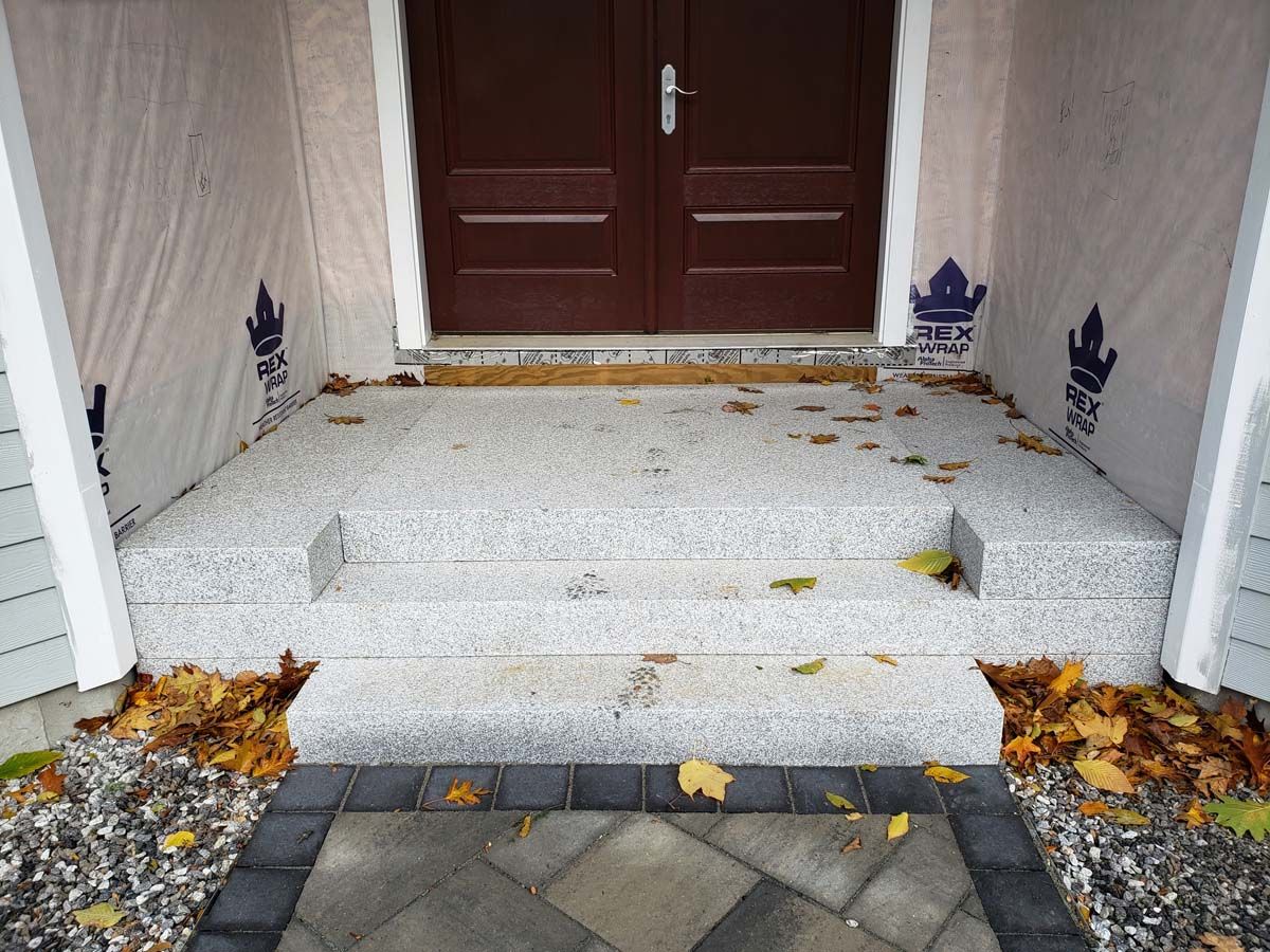Stone steps leading to a brown double door, with scattered leaves and a stone walkway.