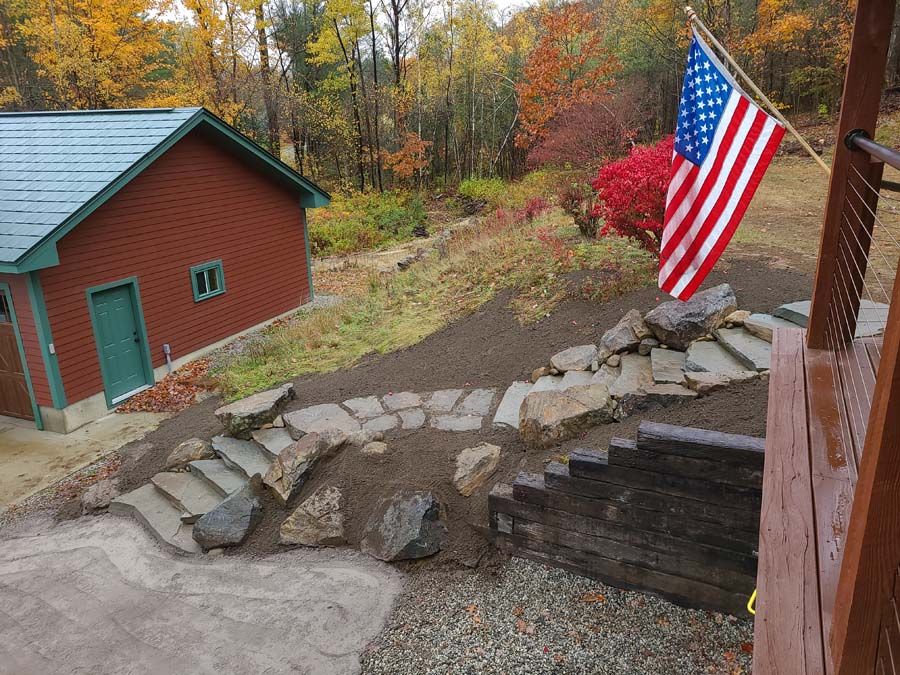 Stone steps and retaining walls lead up to a building with an American flag, set in a wooded area with fall foliage.