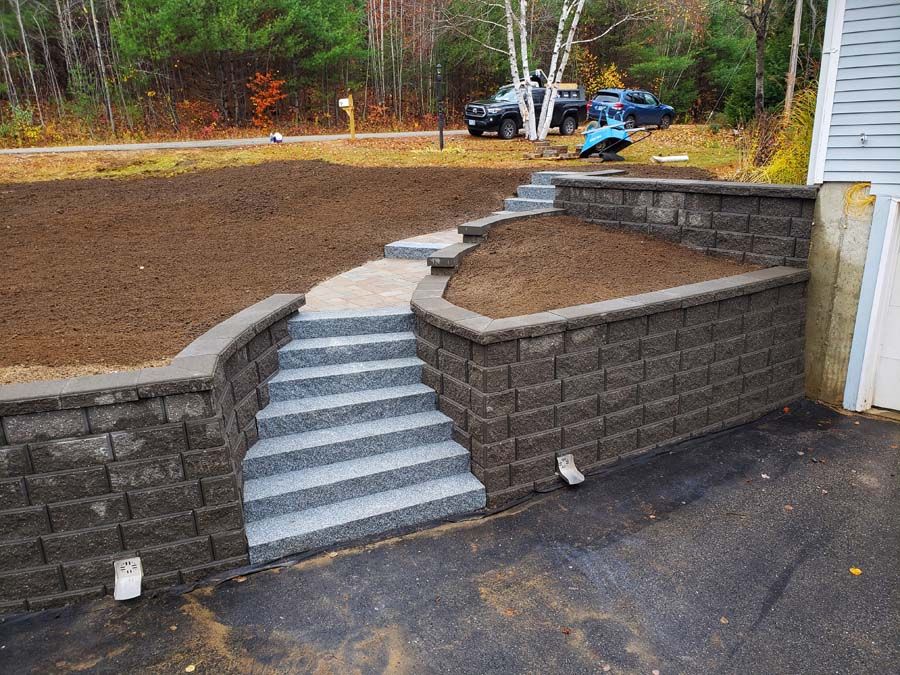 Stone steps and walkway flanked by dark retaining walls, leading up to a graded dirt area.