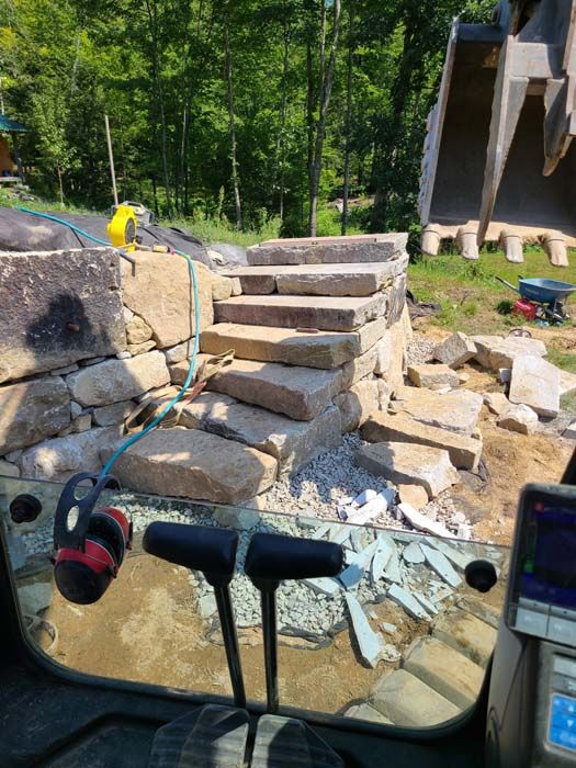 Stone steps being built by heavy machinery in a wooded area.